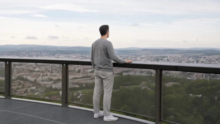 Personne appuyée à une rambarde sécurisée en hauteur, regardant l’horizon d’une ville