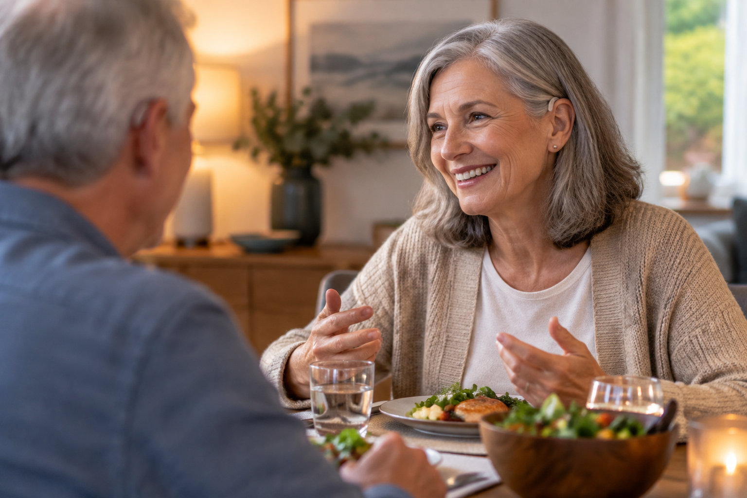 Une femme souriante discute avec un homme autour d’une table dressée, avec des assiettes, des verres et un saladier.